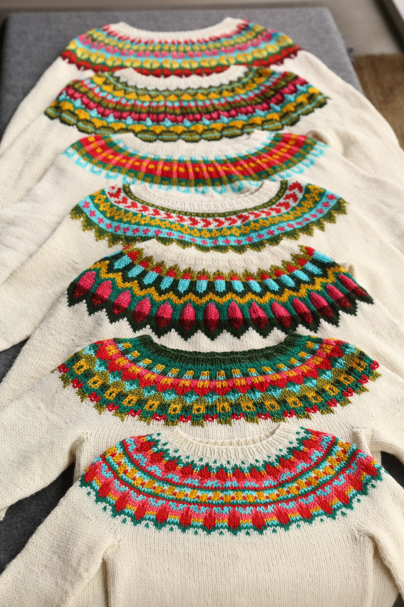 Seven matching yoke sweaters, laid flat.