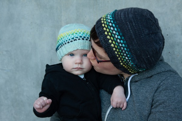 A woman is giving a little baby a kiss on the cheek. They are both wearing hats with a cool ombré band of dots. 